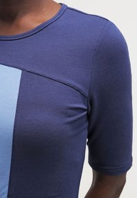 Top z krótkim rękawem z niebiesko-granatowym wzorem kolorystycznym, wykonany z miękkiego, elastycznego materiału o gładkiej fakturze i zaokrąglonym dekolcie.