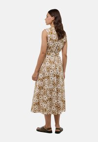 Robe midi sans manches marron avec un motif floral blanc, taille cintrée et jupe fluide. Présente un décolleté droit et un détail de boutons subtil.