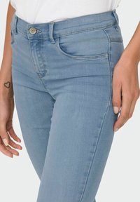 Heled sinise denim kangaga vormitud disainiga teksapüksid, viie taskuga stiil ja peened õmblused. Kangas on sileda tekstuuriga.