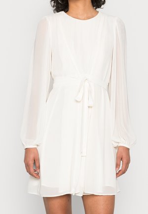 Vestido blanco, fluido, con mangas largas y abullonadas y una cintura ajustable. Confeccionado en una tela ligera, presenta un escote en forma de V y una textura plisada.