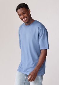 Lyseblå bomulds T-shirt med korte ærmer og rund hals, parret med lyse denim jeans. Glat tekstur og afslappet pasform.