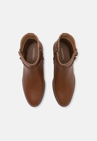 Bottines en cuir marron avec une texture lisse, dotées d'une fermeture éclair sur le côté et d'une garniture en or. Design à bout rond.
