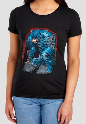 Woman wearing black t-shirt with a graphic of a blue-clad, aggressive Batman character in a dynamic pose.