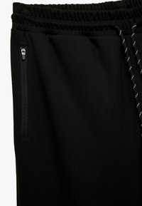 Sorte sweatpants lavet af blød stof, med elastisk talje, justerbar snøre og sidelommer med lynlås og slanke detaljer.