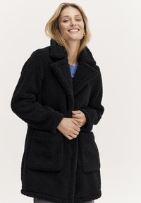 Palton faux fur negru cu guler decupat, mâneci lungi și două buzunare frontale. Oferă un aspect moale și texturat.