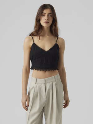 Musta virkattu crop-top, jossa on säädettävät spagettiolkapäät ja kaunis reunus, yhdistettynä vaaleanharmaisiin korkeavyötäröisiin housuihin.