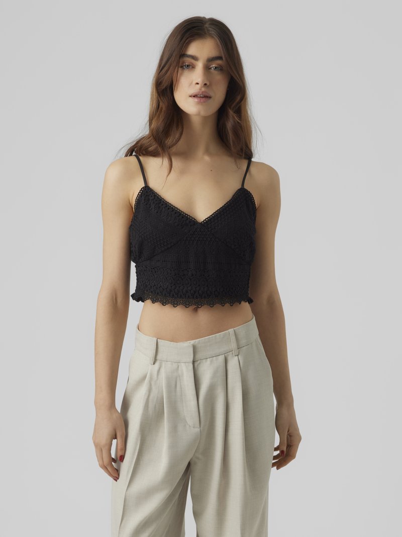 Crni mrežasti crop top s podesivim trakama i valovitim rubom, uparen s svijetlo sivim hlačama visog struka.