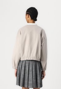 Chaqueta corta gris claro con dobladillos elásticos y mangas abullonadas, combinada con una falda gris plisada que presenta una tela texturizada.
