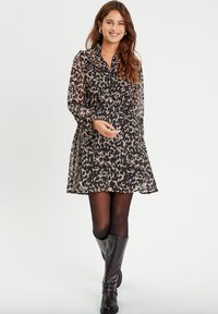 Robe noir et beige à motifs avec de longues manches transparentes, un col boutonné, une taille cintrée et une jupe évasée, accompagnée de bottes noires hautes.
