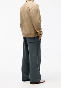 Chaqueta de lona beige con corte recto; combinada con pantalones de pierna ancha grises de una tela suave y texturizada. Zapatos blancos de punta redonda.