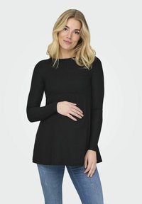 Black ribbed long-sleeve top with a rounded neckline and flared silhouette, paired with light blue distressed jeans.