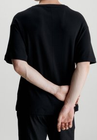 Svart t-shirt med kort ärm, avslappnad passform, rundad halsringning och en slät textur. Baksidan har en sömdetalj. Matchad med mörka byxor.