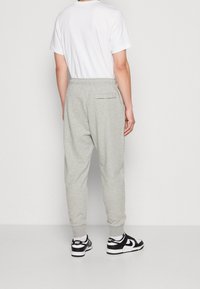 Pantalones jogger de algodón gris con cintura elástica, tobillos ajustados y un bolsillo trasero, combinados con zapatillas negras y blancas.