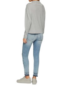 Graues Langarmshirt kombiniert mit hellblauen Skinny Jeans und grauen Sneakern. Die Jeans haben ein ausgewaschenes, distressed Design mit hochgekrempelten Säumen.