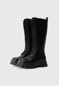 Μαύρες μπότες μέχρι το γόνατο από δέρμα με υφή, διαθέτοντας κορδόνια στο μπροστινό μέρος, στρογγυλή μύτη και χοντρή ελαστική σόλα.