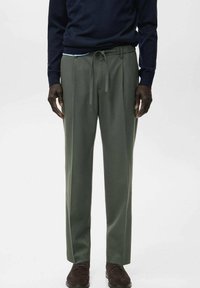 Pantalones verdes de corte relajado, con cinturilla ajustable con cordón, confeccionados en tela suave, combinados con un suéter azul marino y zapatos marrones.