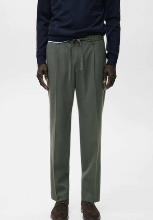 Pantalon vert coupe décontractée, doté d'une ceinture à cordon, fabriqué en tissu doux, associé à un pull bleu marine et des chaussures marron.