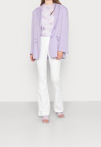 Blazer oversize de lavanda con dos botones, combinado con una camisa de lavanda de tie-dye, pantalones blancos acampanados y sandalias de tacón de lavanda a juego.