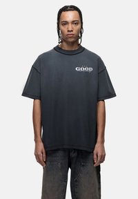 Luźno dopasowana koszulka w ciemnoszarym kolorze z okrągłym dekoltem. Posiada napis "GOOD" w białej konturowej czcionce, krótkie rękawy oraz jest wykonana z bawełny.