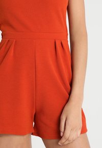 Rode polyester romper met een textuurafwerking, voorzien van een fitted taille en plooien, korte benen en een eenvoudige ronde halslijn.