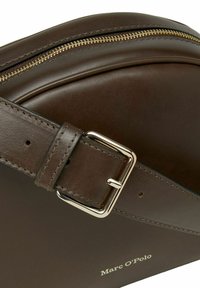 Borsa in pelle marrone scuro con zip dorata e fibbia metallica rettangolare, tracolla cucita e logo "Marc O'Polo" in lettering dorato.