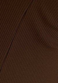 Tissu côtelé brun avec un motif vertical. Le tissu a une texture douce et un éclat subtil, avec un léger élasticité et une bonne drape.