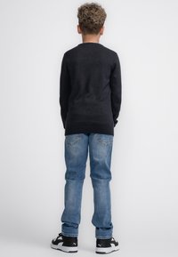 Zwarte trui, lichtblauwe spijkerbroek en zwarte sneakers gezien van achteren. De sweatshirt heeft een ronde halslijn en een slim fit ontwerp.