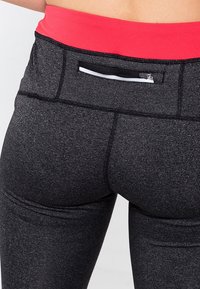 Czarne legginsy sportowe wykonane z rozciągliwego, teksturowanego materiału. Posiadają czerwony wysoki pas w talii oraz małą kieszonkę na zamek z tyłu.
