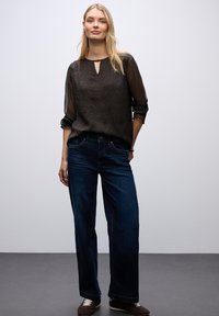 Blusa nera con stampa leopardata e scollatura a forma di chiave, abbinata a jeans blu scuro a vestibilità ampia, esposta su uno sfondo neutro.
