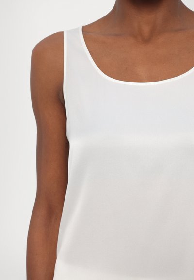 Valkoinen hihaton toppi pyöreällä kaula-aukolla, valmistettu sileästä, kevyestä kankaasta; siinä on hillitty kiilto ja minimalistinen muotoilu.