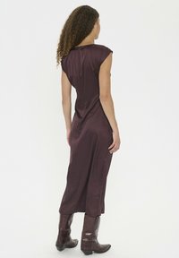 Bordeauxrotes Satin-Kleid mit kurzen Ärmeln und figurbetonter Silhouette, versehen mit einem Schlitz im Rücken und kombiniert mit braunen Leder-Cowboy-Stiefeln.