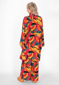 Kolorowy, zwiewny zestaw składający się z kimona i pasujących spodni, zdobiony odważnym wzorem liści w odcieniach czerwieni, zieleni i żółci, wykonany z lekkiego materiału.