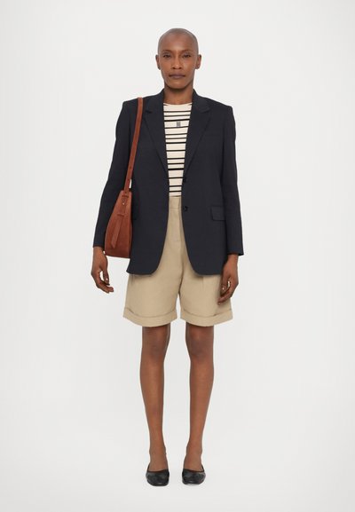 Blazer marine, t-shirt beige à rayures, shorts beige retroussés, sac à épaule marron et ballerines noires. Tissu lisse, design ajusté, look décontracté moderne.