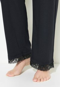 Schwarze Baumwoll-Loungehosen mit zartem schwarzen Spitzebesatz am Saum, der einen texturierten Kontrast zum glatten Stoff bietet.