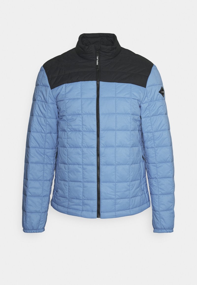 Giacca trapuntata azzurro chiaro con yoke nero sulle spalle, colletto a polo, zip frontale e patch con logo sulla manica sinistra.