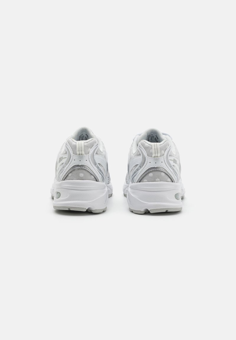 Baskets blanches de sport avec un dessus en maille et synthétique, un col rembourré et une semelle légère avec une adhérence texturée. La vue arrière montre des accents de design uniques.