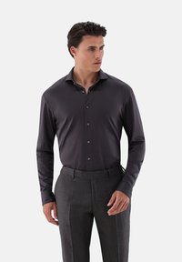 Camicia a maniche lunghe grigio scuro con una texture liscia, bottone frontale, colletto classico e bottoni neri, abbinata a pantaloni grigi con motivo.