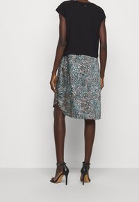 Schwarzes cropped Top mit kurzen Ärmeln, kombiniert mit einem teal- und braun gemusterten Rock, der einen seitlichen Schlitz hat, und schwarzen Absatzsandalen.