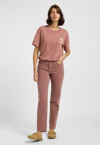 Staubrose T-Shirt mit kleinem Grafikdruck und lässiger Passform, kombiniert mit passenden Slim-Fit-Jeans und beige Slippers.