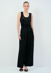 Zwarte mouwloze top met sequins, gecombineerd met hoge zwarte wijde broek en zwarte open teen hakken.