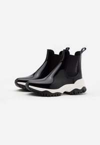 Bottines Chelsea noires brillantes avec semelle en caoutchouc blanche et semelle extérieure texturée noire. Dispose de panneaux latéraux élastiques et d'une languette pour un enfilage facile.