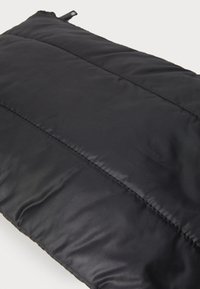 Bolsa acolchada negra hecha de tela suave con costuras visibles y una pequeña pestaña de cremallera. Presenta un diseño texturizado y acolchado.
