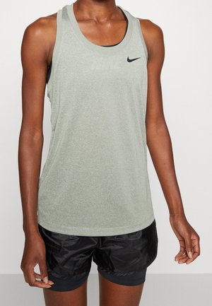 Osoba ubrana w jasnoszary sportowy top bez rękawów marki Nike oraz czarne krótkie spodenki do biegania, stojąca na tle jednolitego białego tła.