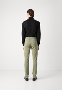 Svart långärmad topp i kombination med ljusgröna byxor. Byxorna har bakfickor; modellen bär svarta skor. Enkelt mönster och modern passform.