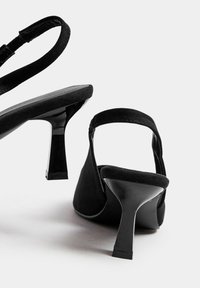 Czarne buty na wysokim obcasie typu slingback, wykonane z zamszu, z błyszczącym obcasem i minimalistycznym designem. Posiadają płaski pasek wokół kostki.