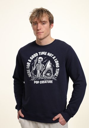 Marine sweatshirt med grafisk tryk, der viser et skelet og en haj, rund halsudskæring, ribbede manchetter og kant, lavet af tekstureret bomuldsstof.
