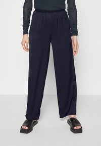 Navy wide-leg trousers with elastic waistband, made of smooth fabric. Paired with chunky black sandals featuring a square toe and platform sole.