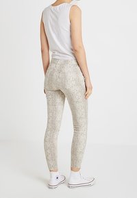 Leggings de estampado de piel de serpiente en beige y blanco con un ajuste elástico, combinados con zapatillas altas blancas y una camiseta ajustada blanca.