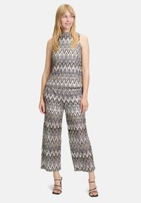 Dwuczęściowy zestaw składający się z topu z wysokim dekoltem bez rękawów i szerokich spodni w falisty czarno-kremowy wzór. Materiał wydaje się lekki.