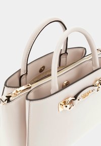 Borsa a mano beige chiaro con doppie maniglie, hardware dorato, chiusura a zip e placchetta con logo. Texture liscia con bordo scuro.